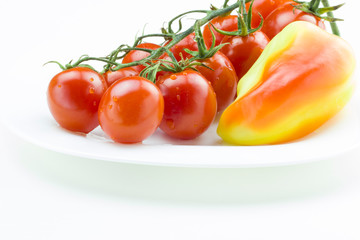 Bunch of fresh red tomatoes and yellow sweet pepper on a plate Close up view, white background. Healthy food concept.