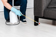 © LIGHTFIELD STUDIOS - cropped view of man in uniform and blue latex gloves holding spray with pesticide near sofa