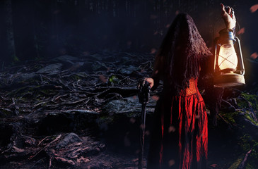 Horror halloween female forest witch in red dress standing with lantern and cane.