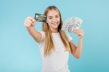 smiling young woman with credit card and dollars money in her hands isolated over blue