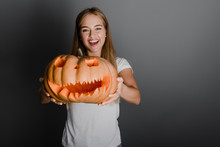 Playful Funny Blonde Girl With Halloween Jack O Lantern Pumpkin Isolated Over Grey