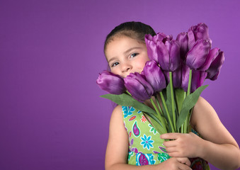 Cute little girl peeking from behind bouquet of  tulips isolated on purple background