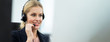 © Kawee - Beautiful Caucasian female call center with headset talking to customer in office. The girl working as technical service support. Seen behind the back of computer monitor in banner size.