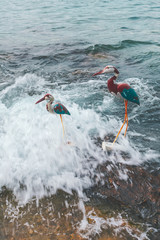 View of two colorful handmade bird or heron figurines on a rock in the sea, mediterranean decoration, Vis island, Croatia, Europe. Vintage toned.