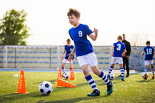 Kids Sports: Teaching Children To Improve Soccer Skills. Football Camp For Kids. Boys Practice Dribbling In Field. Players Develop Skills. Children Training With Balls And Cones. Soccer Slalom Drills
