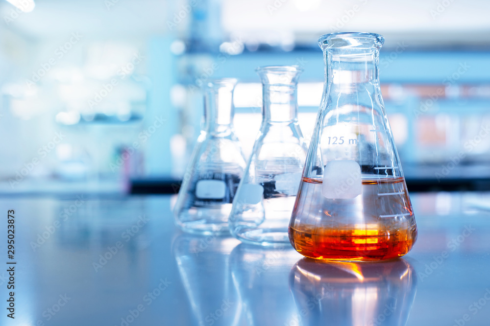 orange solution in science glass flask in blue chemistry school laboratory background - obrazy, fototapety, plakaty 