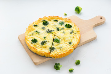 Homemade tart with broccoli and cheese on a white table.