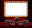 Man sitting in front of lighted sign on red theatre curtain
