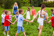 © oksix - Group of children holding hands and dancing in circle on green lawn in park