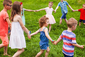 Wall Mural - Happy friends doing circle dance on green grass in summer day.