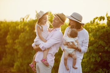 Young family with children having fun in nature on summer sunset background. Mother and father hugs his two little daughters 