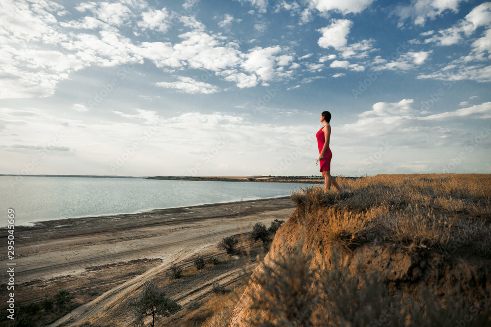 Girl in a red dress is looking at the beautiful scenery of lake coast ...