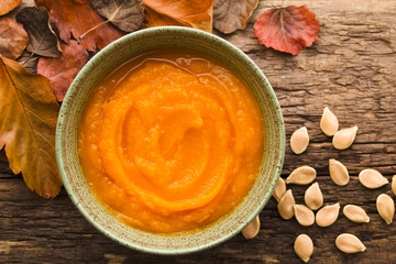 Wall Mural - Fresh homemade pumpkin puree in bowl, colorful autumn leaves and pumpkin seeds on the side, photographed overhead (Selective Focus, Focus on the dish)
