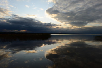 Wall Mural - Clouds in the blue sky reflect on the calm clear water of the lake on sunset