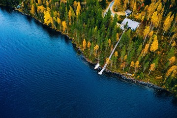 Aerial view of cottage in autumn colors forest by blue lake in rural Finland