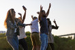 Smiling young people dancing with raised hands in park. Happy young friends listening music and dancing. Leisure concept