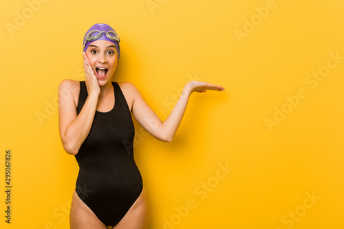 Fotografía Young swimmer caucasian woman holds copy space on a palm, keep hand over cheek