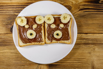 Two sweet sandwiches with delicious chocolate hazelnut spread and banana in shape of bear on wooden table. Top view