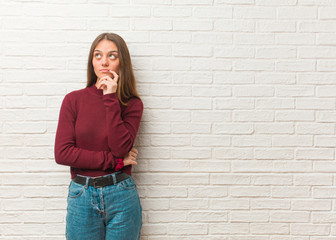 Young cool woman over a bricks wall doubting and confused