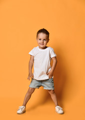 Canvas Print - Happy smiling kid boy in white t-shirt and blue jeans shorts is looking straight in camera on yellow free copy space