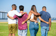 © Mangostar - Team of friends embracing outside. Backs of young men and woman standing in line on grass, hugging each other. Friendship or unity concept