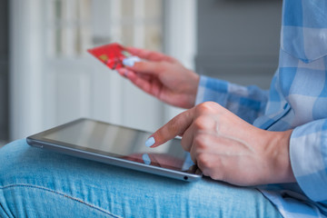 Woman using black digital tablet device and entering security code of red credit card. Online shopping, buying, e-commerce, sale, consumerism, internet shop, electronic payment, technology concept