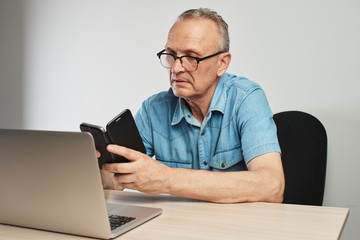 Wall Mural - Elderly Caucasian man in glasses with a serious expression on his face working on a laptop at his desk on a white background