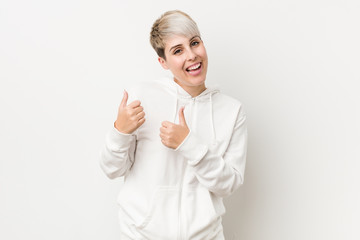 Wall Mural - Young curvy woman wearing a white hoodie raising both thumbs up, smiling and confident.