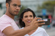 © Mangostar - Happy multiracial couple taking self portrait with phone. handsome African American man holding smartphone in outstretched arm. Concept of self portrait