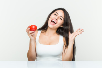 Young hispanic woman holding a tomato celebrating a victory or success