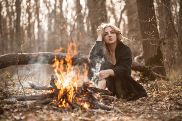 Young woman sitting near bonfire in autumn forest