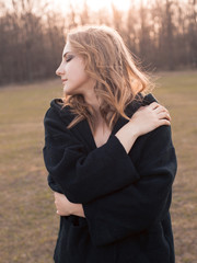 Wall Mural - A young woman in black clothes posing outdoors at sunset