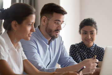 Poster - Serious caucasian teacher instructing diverse students explaining computer project