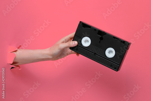 Fotomural Female hand holds video cassette through torn pink paper background