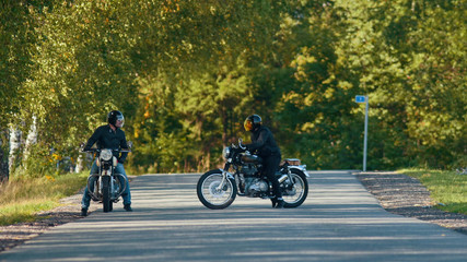 Two bikers on their bikes are standing near each other on the road