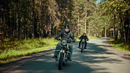 Two bikers are on their bikes riding too fast on the road in forest