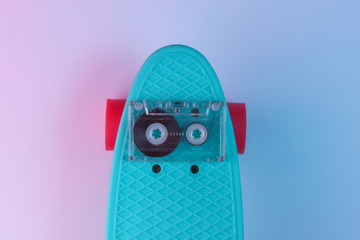 Retro 80s objects. Plastic mini cruiser board and audio tape on background with blue pink neon gradient ligh. Top view