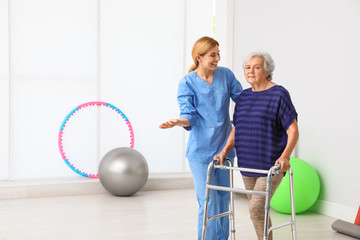 Canvas Print - Caretaker helping elderly woman with walking frame indoors