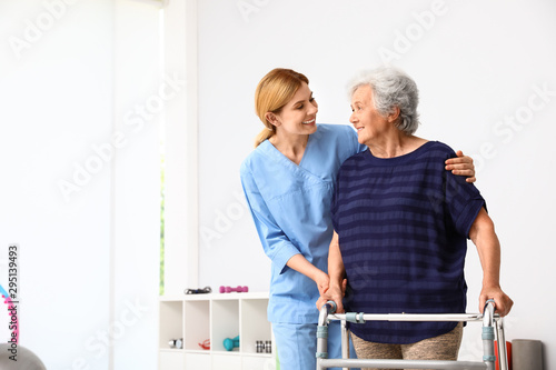 Cuadros en Lienzo Caretaker helping elderly woman with walking frame indoors