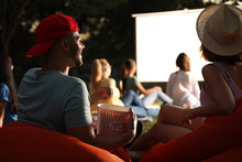 Young Couple With Popcorn Watching Movie In Open Air Cinema. Space For Text