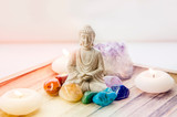 All seven chakra colors crystals stones around sitting Buddha figurine on natural wooden tray. Balance and calm energy flow in home concept.