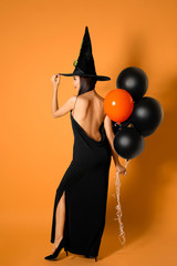 Wall Mural - Beautiful woman wearing witch costume with balloons for Halloween party on yellow background