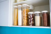 Stocked Kitchen Pantry With Food - Pasta, Buckwheat, Rice And Sugar , Side View. The Organization And Storage In Kitchen Of A Case With Grain In Plastic Containers.