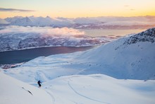 High Angle Shot Of A Mountain Range Covered In Snow Near The Lake And People Skiing
