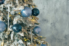 Christmas Interior Decor. Cropped Shot Of Green Fir Tree With Snow, Shiny Blue Glass Ball Ornaments And Fairy Lights. Copy Space.