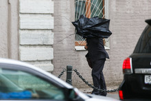 A Man With An Umbrella Is Hiding From Strong Winds And Rain