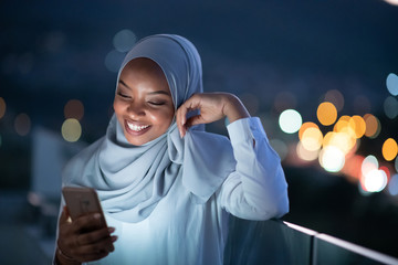 Young Muslim woman on  street at night using phone