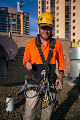 Wall Mural - Happy industrial rope access wearing standard PPE yellow hard hat, long sleeve shirt, full body safety harness accessory equipment prior to descend top high rise building circular quay, Sydney CBD