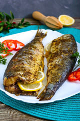 Wall Mural - Baked herring with lemon and spices on a white plate on a wooden table. Tasty fish dish. Top view.