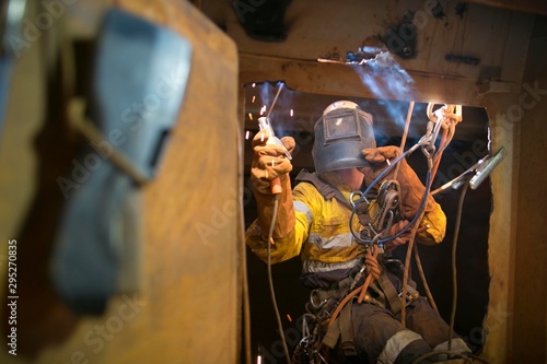 Rope access welder wearing fully safety uniform fall protection helmet, welding glove harness, commencing welding chute repair in confined space construction mine site Perth Pilbara region Australia
